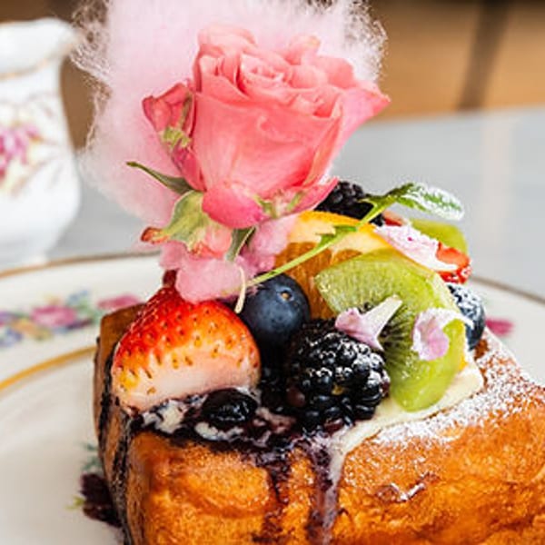 Thick French toast topped with fresh berries, kiwi, a pink rose, and cotton candy.