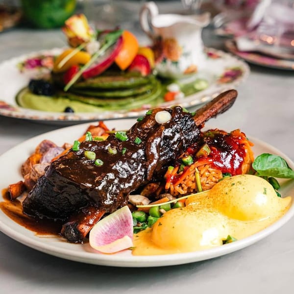 Braised short rib with poached eggs, rice, and vegetables, with green pancakes in the background.