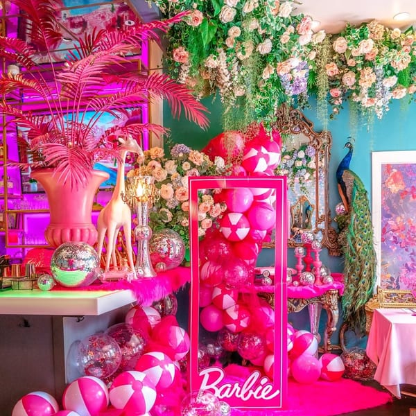 A vibrant Barbie-themed display with pink decor, balloons, disco balls, and a peacock.