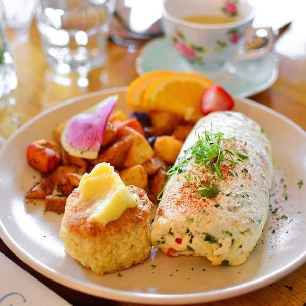 A breakfast plate with an omelet, scone with butter, roasted potatoes, and fruit slices.