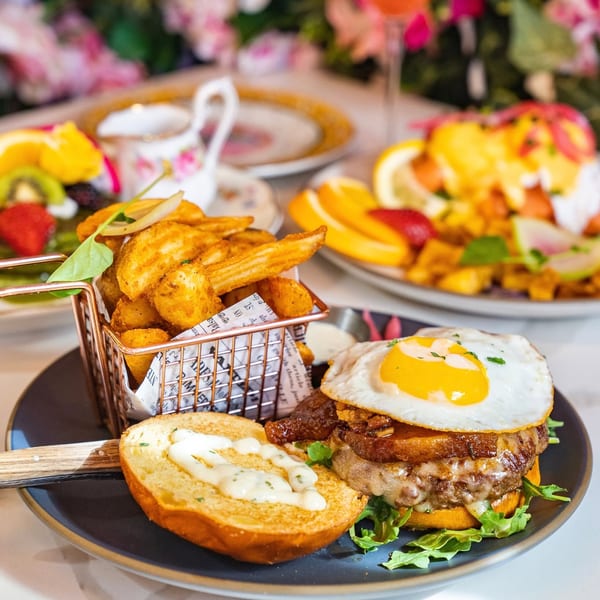 A gourmet burger with a fried egg and bacon, served with a side of crispy potato wedges.
