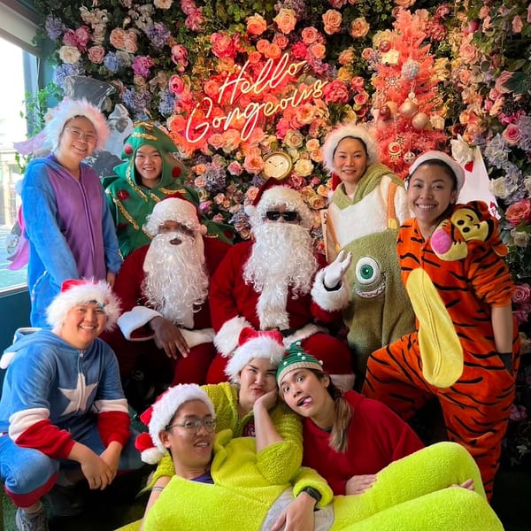 Two Santas and a group of friends in festive costumes pose in front of a floral wall.