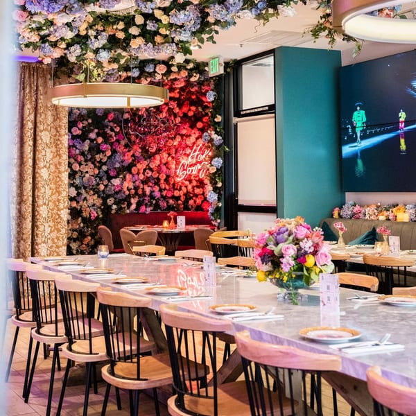 A vibrant restaurant interior with a long dining table, floral ceiling, and a neon sign.