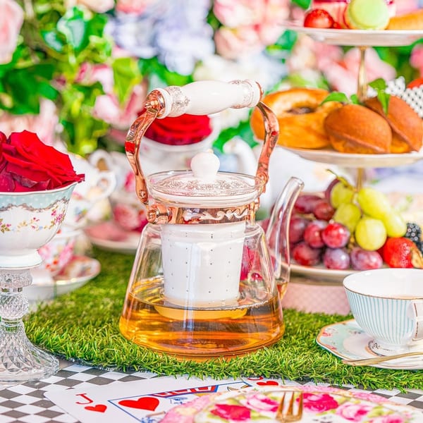 A whimsical Alice in Wonderland-themed tea party with a teapot, desserts, fruit, and floral decor.