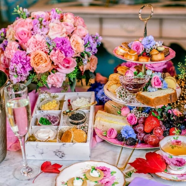 A vibrant afternoon tea spread with a three-tiered stand of pastries, sandwiches, fruits, and flowers.