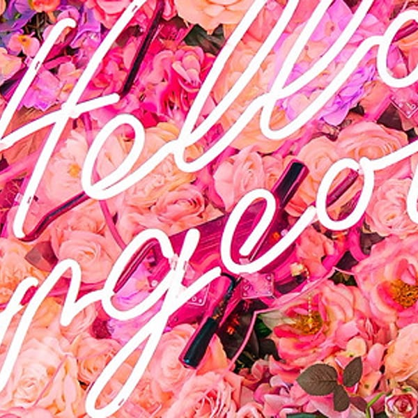 Neon sign spelling "Hello Gorgeous" on a vibrant wall of pink, peach, and blue flowers.