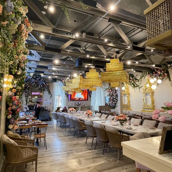 Elegant restaurant interior with long dining tables, floral decor, and ornate golden chandeliers.