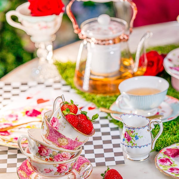 A whimsical tea party setup with stacked floral teacups, fresh strawberries, and a teapot.
