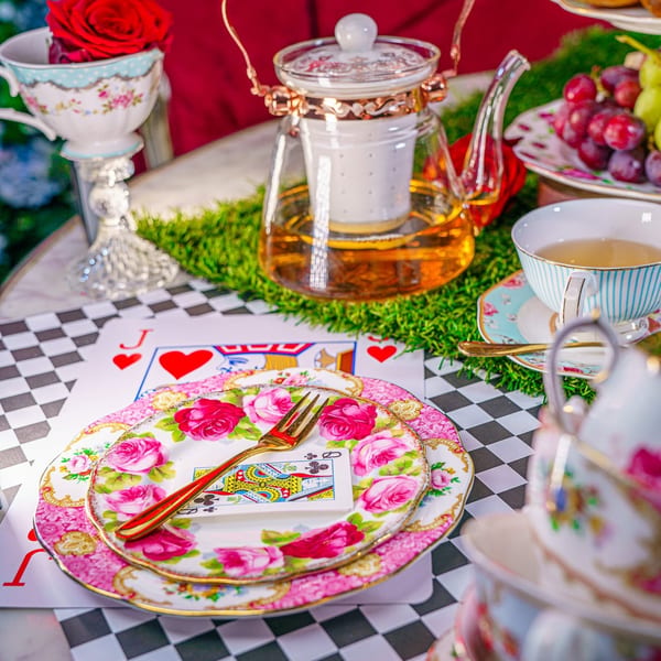 A whimsical Alice in Wonderland tea party setting with playing cards, floral plates, and teapots.