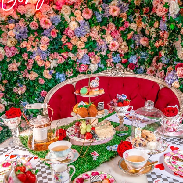 An Alice in Wonderland-themed tea party with desserts, sandwiches, and a "Hello Gorgeous" neon sign.